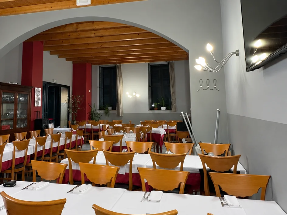 Seconda veranda del ristorante: soffitto in travi di legno, arco centrale, TV a parete e tavoli apparecchiati con tovaglie bianche