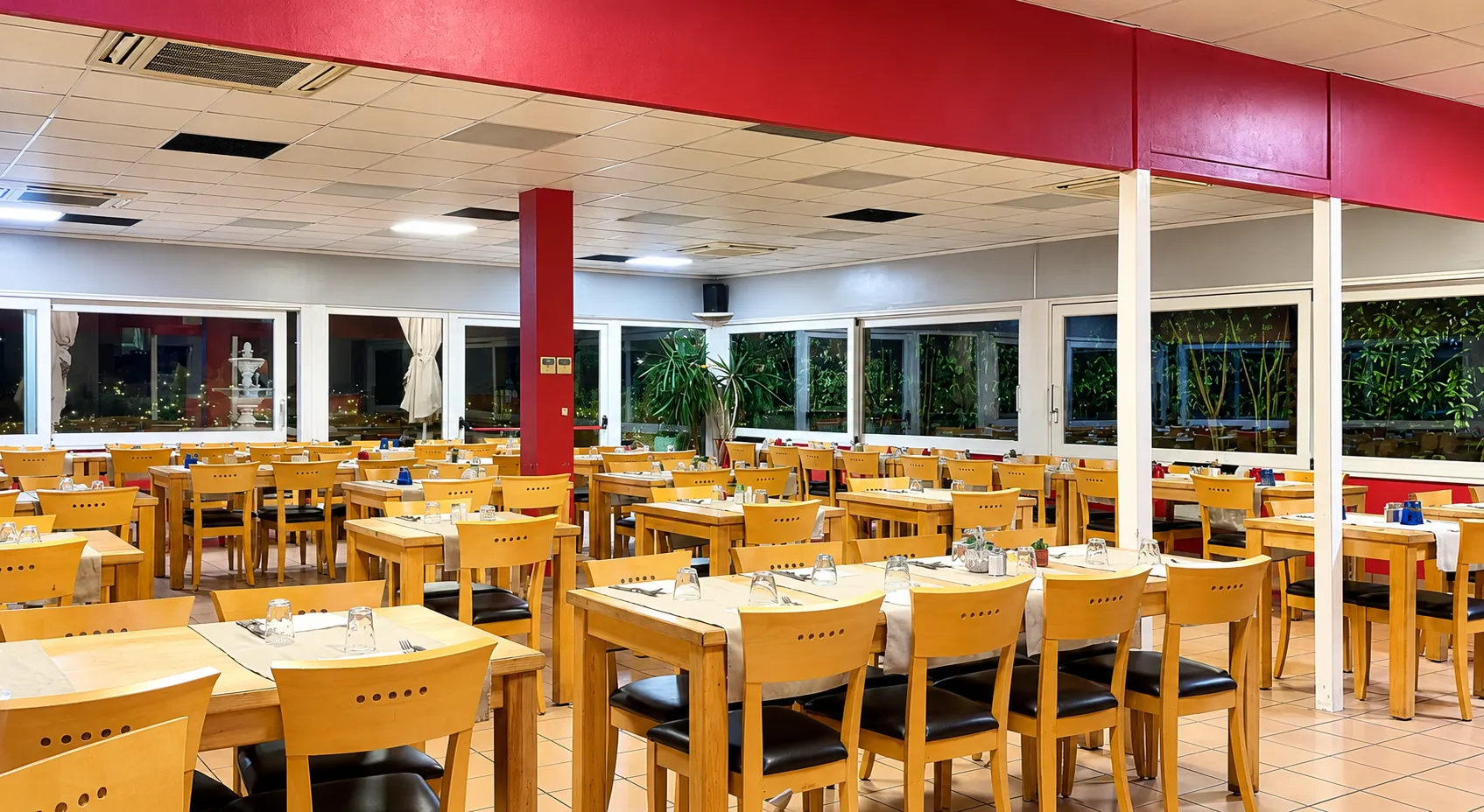 Veranda interna del ristorante con i tavoli apparecchiati e le vetrate sul giardino