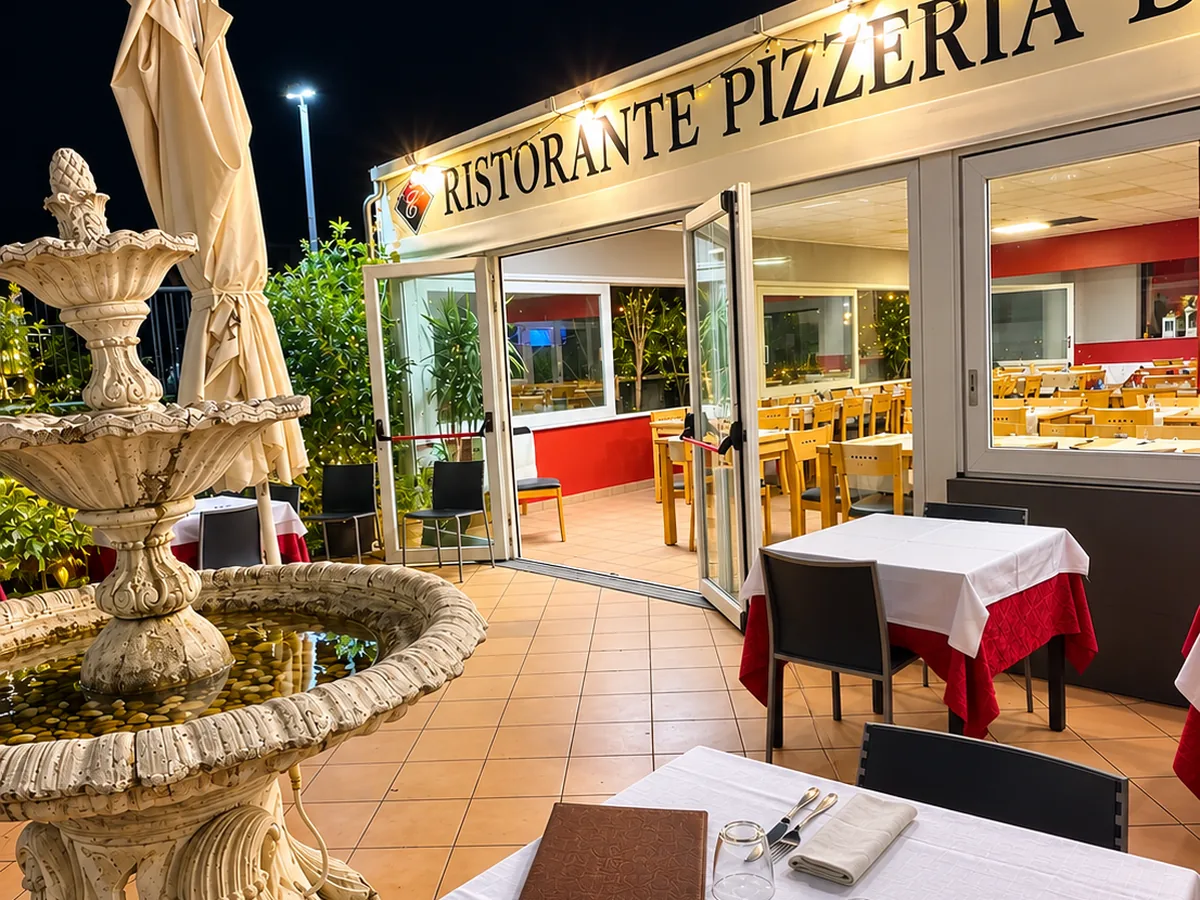 Veranda esterna di sera con l'insegna Ristorante Pizzeria, la fontana e i tavoli apparecchiati